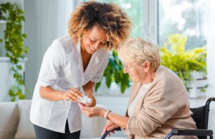 Afro American female home nurse giving medicine to the senior woman. An elderly lady sitting in an armchair.
