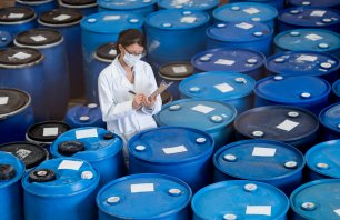 Woman working at a chemical plant wearing a facemask and writing on a clipboard while doing an inventory