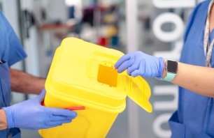 Medical professional safely discarding used syringe in designated sharps container, highlighting proper biohazard waste management in healthcare